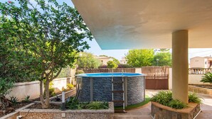 A swimming pool with a stone exterior, surrounded by a garden with various plants and a tree. - Amazing home in Porto Cristo (Porto Cristo)
