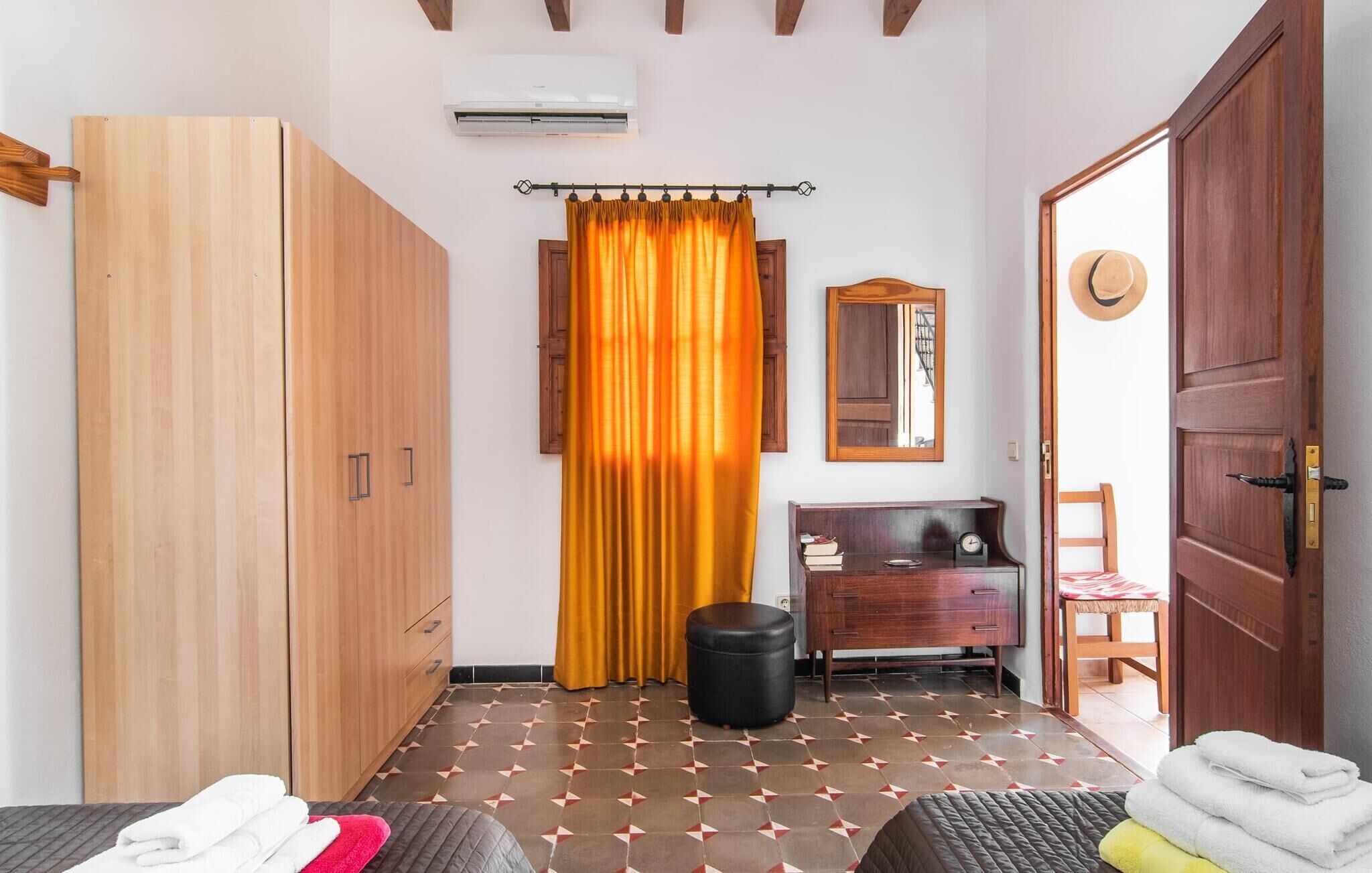 A room with a bed, a wardrobe, a small table with a clock, a mirror, and a door.