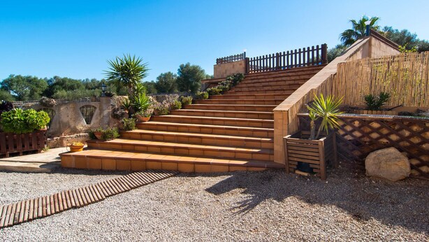 Una escalera que sube hacia un edificio con una valla de madera y macetas con plantas.