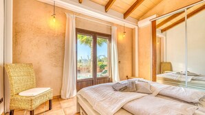 A bedroom with a large bed, a wicker chair, a glass door leading to a pool, and a wooden ceiling. - Luxurious home in Campos with private swimming pool, can be inside or outside (Campos)