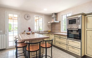 A kitchen with a central island, two bar stools, a clock, a stove, and a microwave. - Cozy home in Palma with private swimming pool, can be inside or outside (Palma)