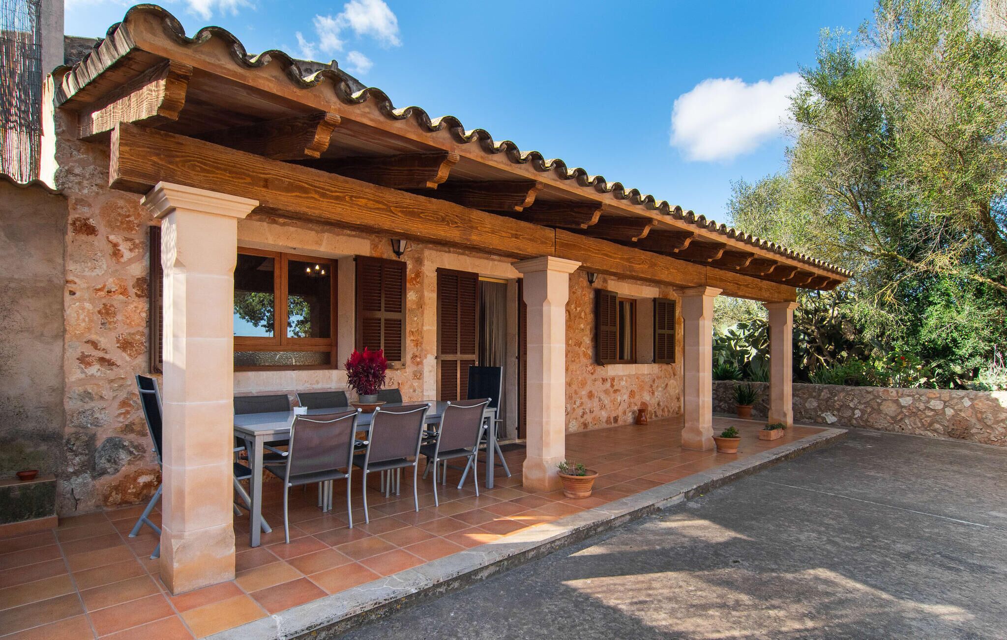 Un bâtiment en pierre doté d’une terrasse carrelée, de sièges en plein air et d’une pergola.