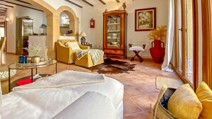 A spacious living room with a sofa, armchairs, a coffee table, and a fireplace. There is a dining area with a table and chairs, and a kitchen visible through an archway. - Nice home in Arta with private swimming pool, can be inside or outside (Arta)