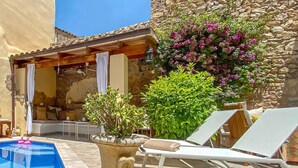 A pool area with lounge chairs, a stone wall, and flowering plants. - Nice home in Arta with private swimming pool, can be inside or outside (Arta)