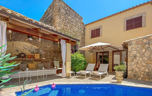Un espace piscine aménagé avec des chaises longues, un mur en pierre et une piscine carrelée.