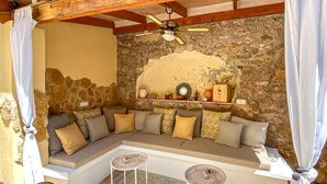 A cozy seating area with a stone wall backdrop, a ceiling fan, and a shelf with decorative items. - Nice home in Arta with private swimming pool, can be inside or outside (Arta)