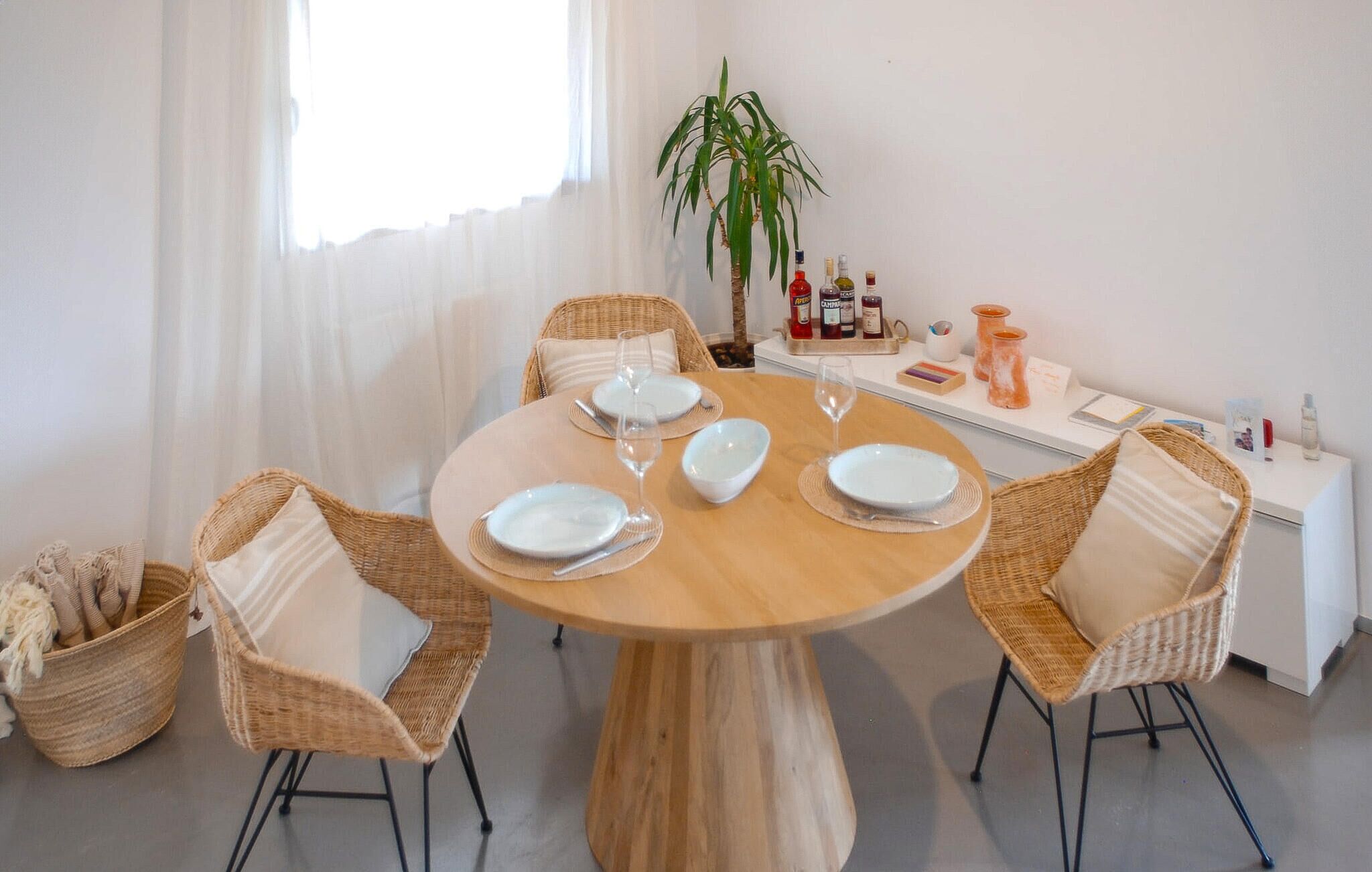 A dining area with a round table set for four, surrounded by wicker chairs.