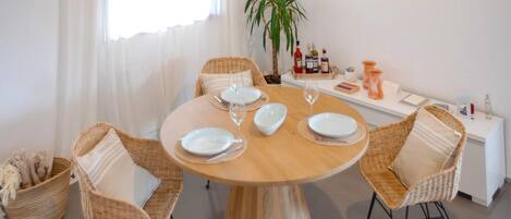 A dining area with a round table set for four, surrounded by wicker chairs.