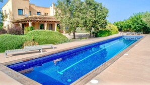 Ein rechteckiger Pool mit einer gefliesten Kante, umgeben von einer Holzterrasse. Liegestühle und eine kleine Brücke über dem Pool sind vorhanden.