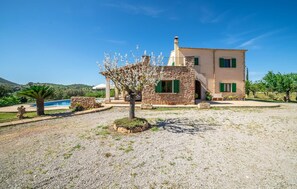 Une maison en pierre à deux étages, dotée d’une piscine, entourée d’une allée en gravier et de verdure.