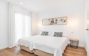 A double bed with a white quilt, two pillows, a small round table, and a wall art piece above the bed. - Petit Arta - Sa Botigueta (Arta)
