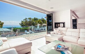 A modern living room with a glass wall overlooking a scenic view of the sea and a statue. - Gorgeous home in Palma with sauna (Palma)