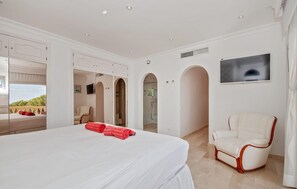 Ein Hotelzimmer mit einem großen Bett, einem weißen Sessel und einem Fernseher an der Wand.