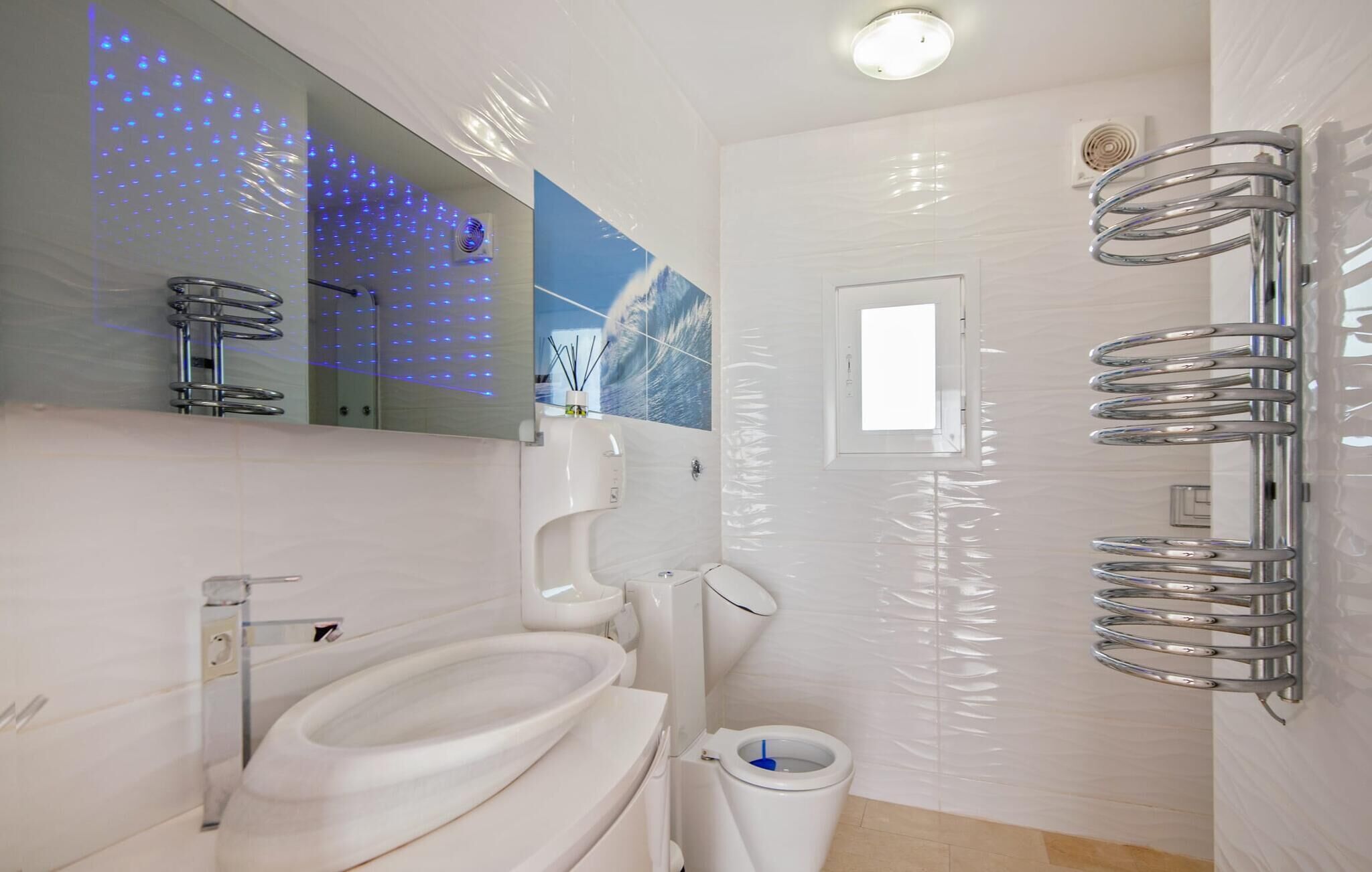 Une salle de bain moderne avec des toilettes blanches, un lavabo et un miroir. On y trouve également une zone douche avec une porte en verre et un porte-serviettes.