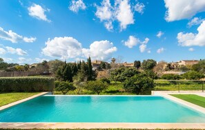 A rectangular swimming pool with a clear blue water surface, surrounded by well-maintained grass and hedges, with a backdrop of a clear sky and distant buildings. - Luxurious home in Ariany with private swimming pool, can be inside or outside (Ariany)