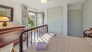 Ein Schlafzimmer mit Bett, Kommode, Deckenventilator, Fenster mit Vorhängen und einer Tür.