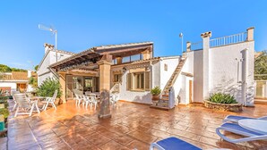 Eine Villa mit Terrasse, Sitzgelegenheiten im Freien und einer Treppe zum Obergeschoss.