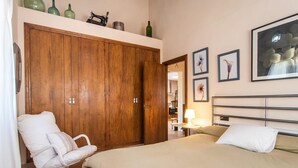 A bedroom with a wooden wardrobe, a bed with beige bedding, a white chair, and framed floral artwork on the wall. - Nice home in Campanet with private swimming pool, can be inside or outside (Campanet)