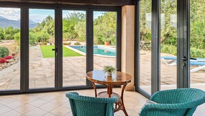 A room with a glass door leading to a pool and garden, two wicker chairs, and a small table with a plant. - Nice home in Campanet with private swimming pool, can be inside or outside (Campanet)