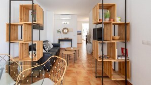 A modern living room with a sofa, coffee table, and a dining area. There are wooden shelves with plants and books. - 2 bedroom gorgeous apartment in Arta (Arta)
