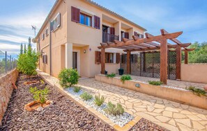 Ein zweigeschossiges Haus mit überdachter Terrasse, einem Kiesweg und einem kleinen Garten.