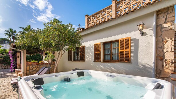 Un'area benessere con vasca idromassaggio, pareti in pietra, persiane di legno e un balcone decorativo.