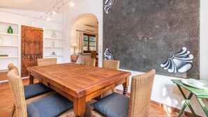 Zona pranzo con tavolo in legno, sedie in vimini e un grande quadro astratto appeso al muro.
