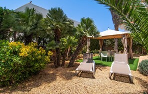 A garden with two lounge chairs, a table, and a covered seating area. - Casa Angela III Jardin (Cala Ratjada)