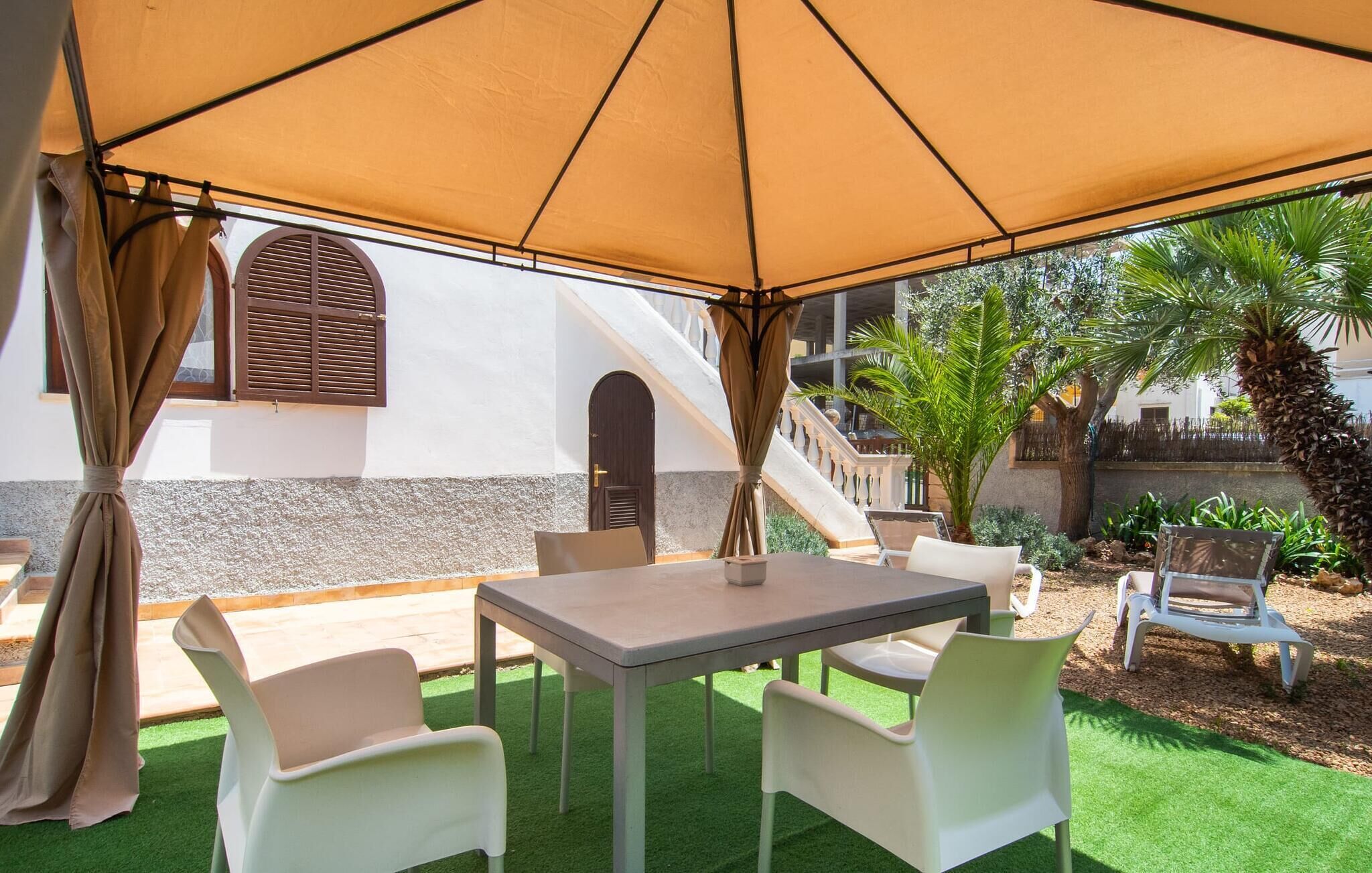 An outdoor patio with a table and chairs under a large canopy, a staircase, and a view of a building with a window and shutters.