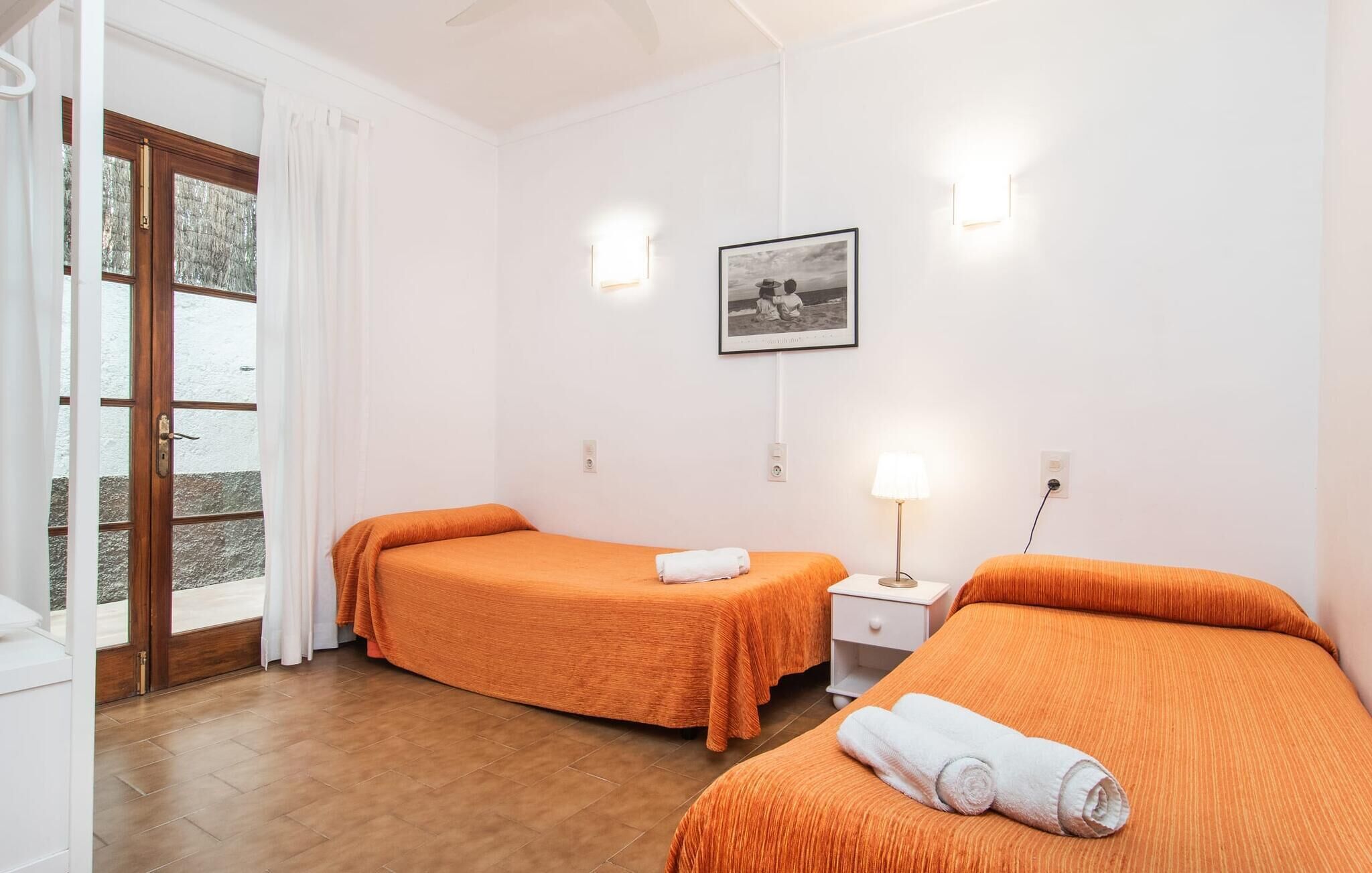 A hotel room with two beds, a small bedside table with a lamp, a framed picture on the wall, and a sliding glass door leading to an outdoor area.