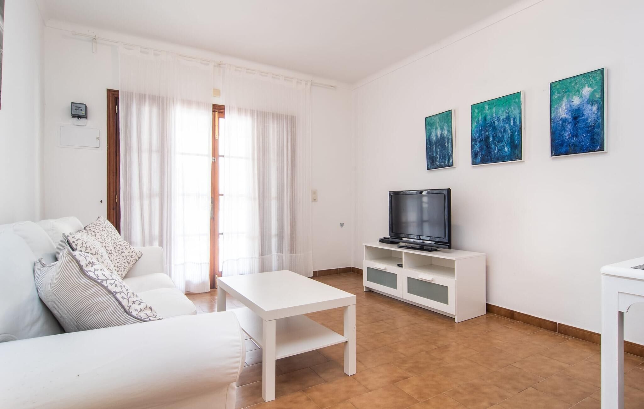 Una sala de estar moderna con un sofá blanco, una mesa de centro, un televisor sobre un mueble blanco y tres cuadros abstractos en la pared.