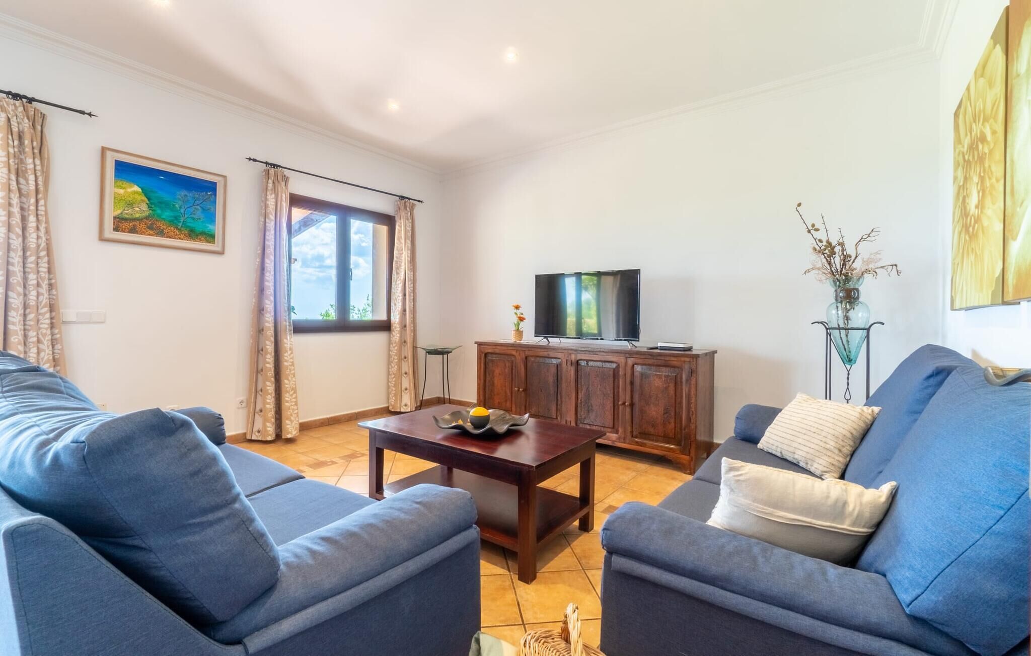 A living room with a sofa set, a wooden coffee table, a TV on a cabinet, and a window with curtains.