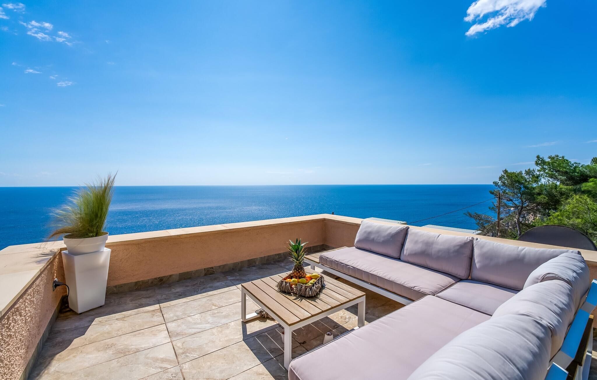 Une terrasse avec un canapé, une table garnie de fruits et une vue sur la mer.