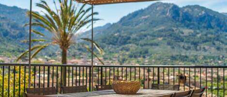 A table with chairs and a woven basket on a terrace with a mountain view.
