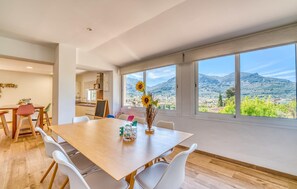 Ein moderner Essbereich mit einem großen Tisch, weißen Stühlen und Blick auf eine Berglandschaft durch große Fenster.