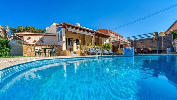 A swimming pool with lounge chairs, a stone wall, and a building with a tiled roof. - Gorgeous home in Alcudia with private swimming pool, can be inside or outside (Alcudia)