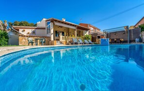 Una piscina con lettini, un muro in pietra e un edificio con tetto in tegole.