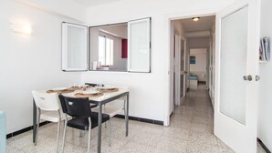 Ein kompaktes Hotelzimmer mit Essbereich, ausgestattet mit einem Tisch für zwei Personen, einem schwarzen und einem weißen Stuhl. Das Zimmer verfügt über eine weiße Tür, einen kleinen Flur, der zu einem weiteren Raum führt, und einen wandmontierten Spiegel.