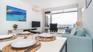 Ein modernes Wohnzimmer mit Essbereich, Fernseher und einem großen Fenster mit Meerblick.