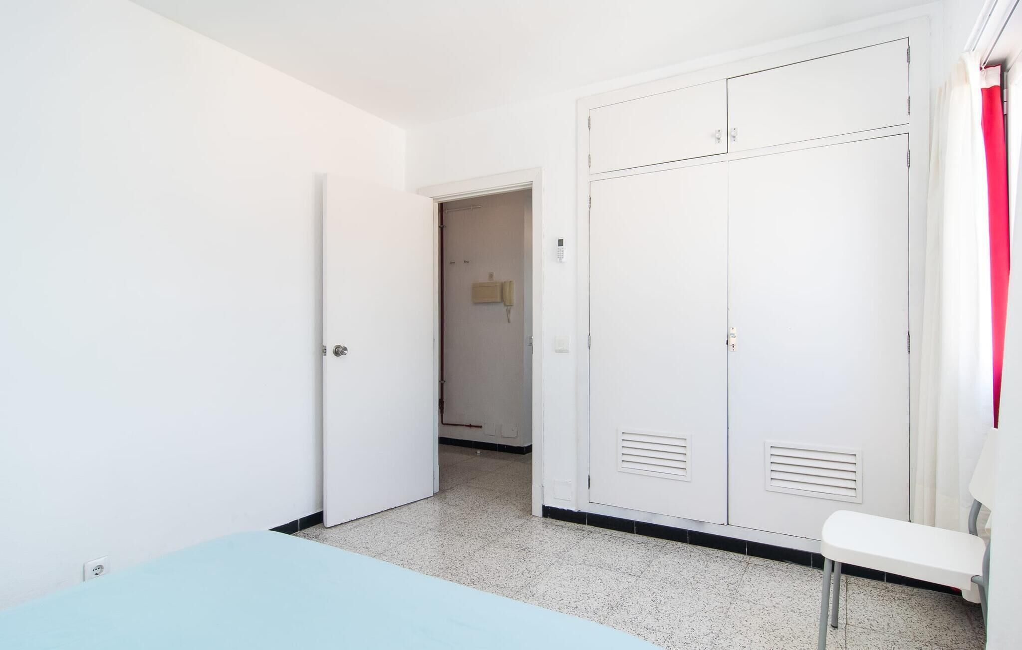 Une pièce comprenant un lit, une armoire, une petite table et une porte donnant sur une autre pièce.