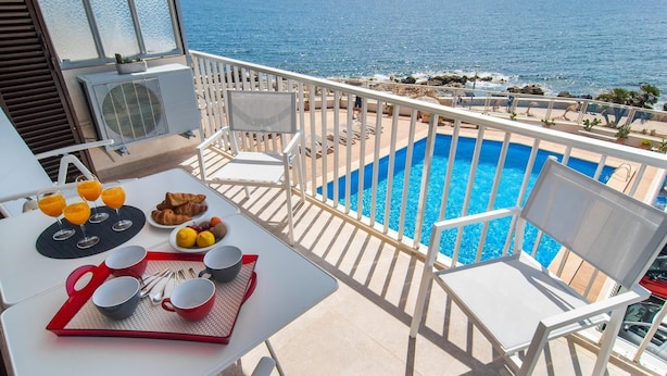 Ein Balkon mit Pool, weißen Stühlen und einem Tisch mit Frühstück.