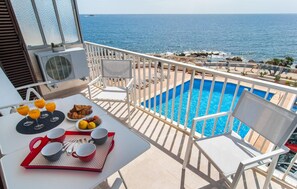 A balcony with a pool, white chairs, and a table with breakfast items. - Gorgeous apartment in Cala Ratjada with outdoor swimming pool (Cala Ratjada)