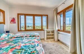 Ein Schlafzimmer mit Bett, einem Fenster mit Blick auf Grünflächen, einem Heizkörper und einem Schrank mit dekorativen Kacheln.