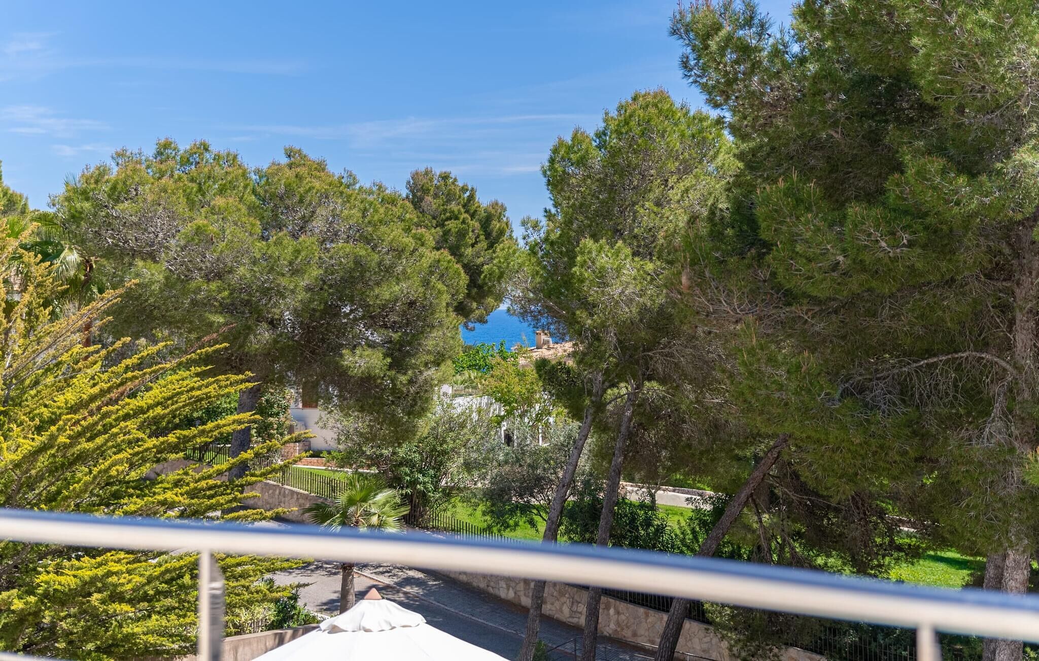 A balcony with a view of a coastal area, trees, and a clear sky.