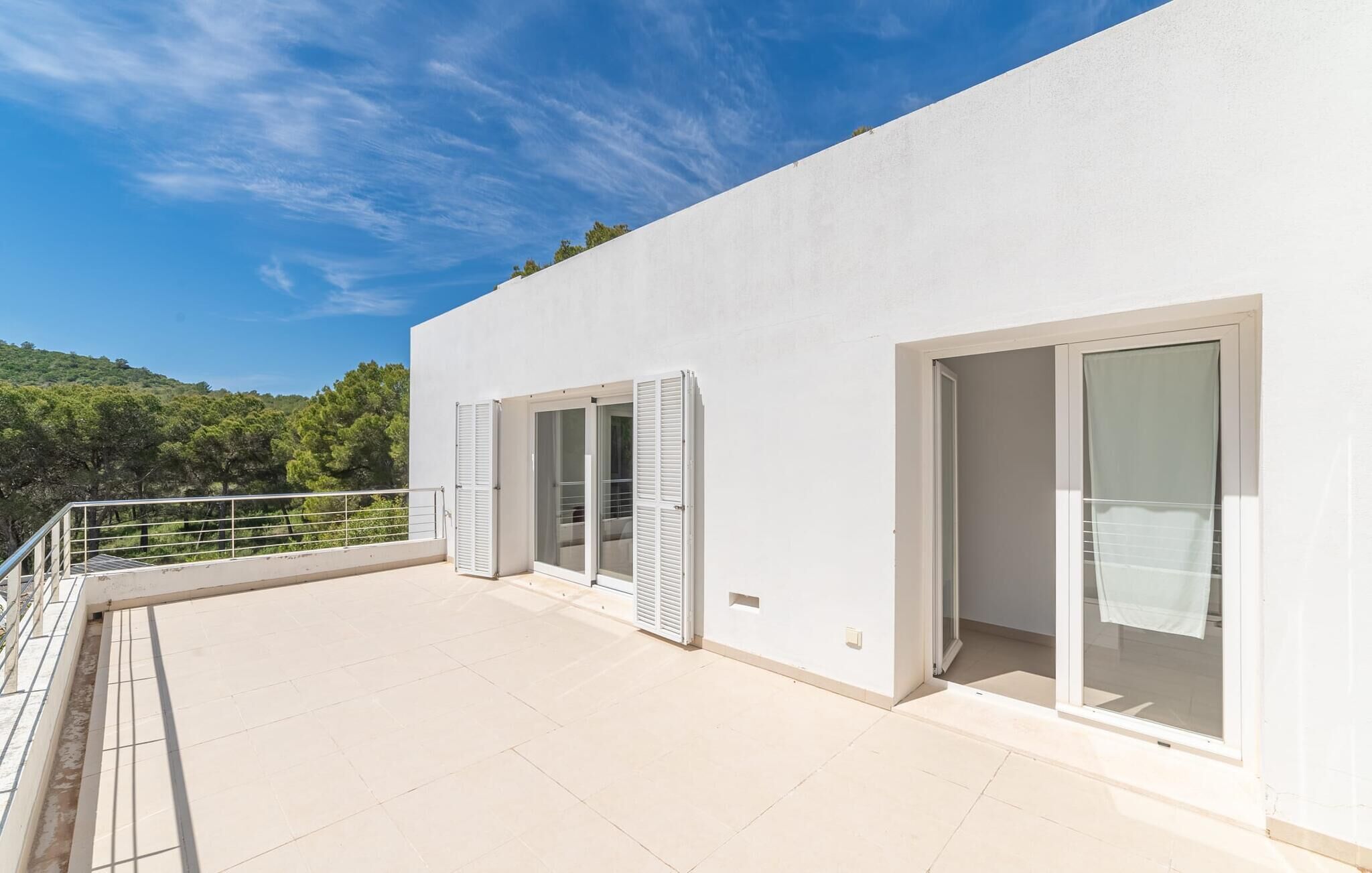 Un bâtiment moderne doté d’un toit plat, de grandes portes-fenêtres coulissantes et d’un balcon avec une rambarde en métal.