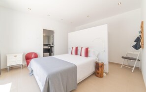 A modern bedroom with a large bed, a red chair, a white dresser, and a wooden stool. - Beautiful home in Sa Font de Sa Cala (Sa Font de Sa Cala)