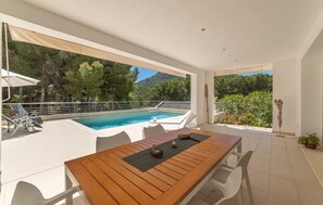 A modern outdoor pool area with a wooden table and chairs, surrounded by a white fence and overlooking a mountainous landscape. - Beautiful home in Sa Font de Sa Cala (Sa Font de Sa Cala)