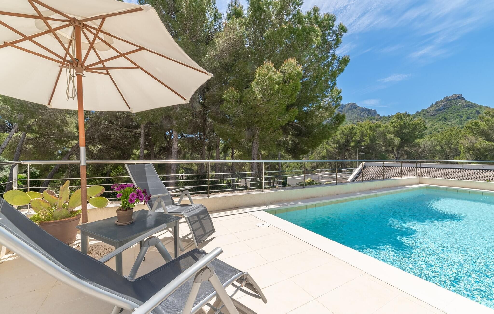 A pool area with lounge chairs and an umbrella, surrounded by trees and a mountainous backdrop.