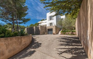 A modern two-story building with a stone facade, a garage, and a paved driveway leading to a gated entrance. - Beautiful home in Sa Font de Sa Cala (Sa Font de Sa Cala)
