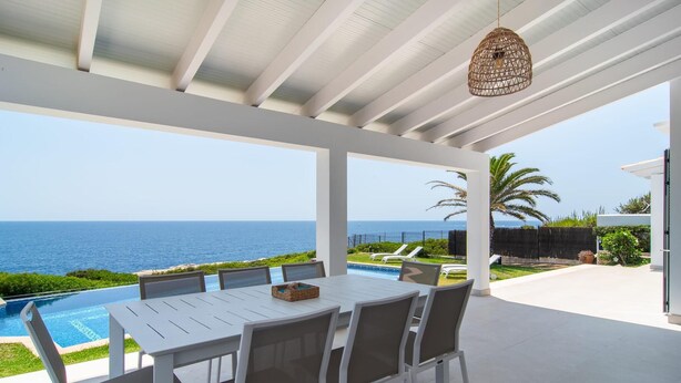 Un'area pranzo all'aperto coperta con vista sull'oceano, una piscina e un patio con poltrone prendisole.